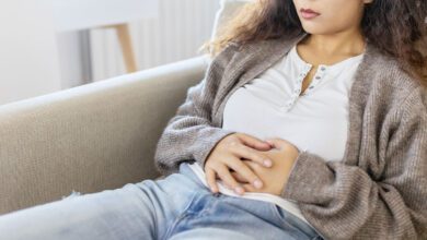 Woman In Discomfort Holding Her Stomach On The Couch Cryptic Pregnancy.jpg