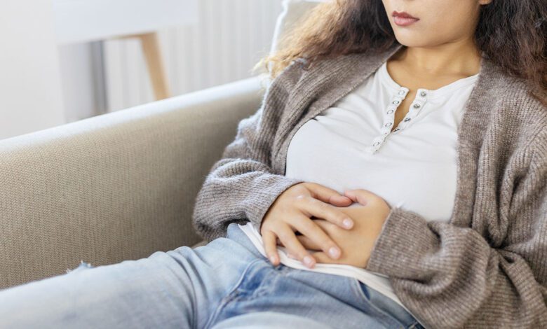 Woman In Discomfort Holding Her Stomach On The Couch Cryptic Pregnancy.jpg